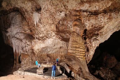 Three people stand on a platform in the Big Room cavern at Carlsbad Caverns National Park