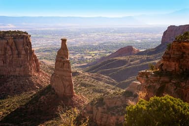 Column of rock with a city and mountains in the distance at Colorado National Monument
