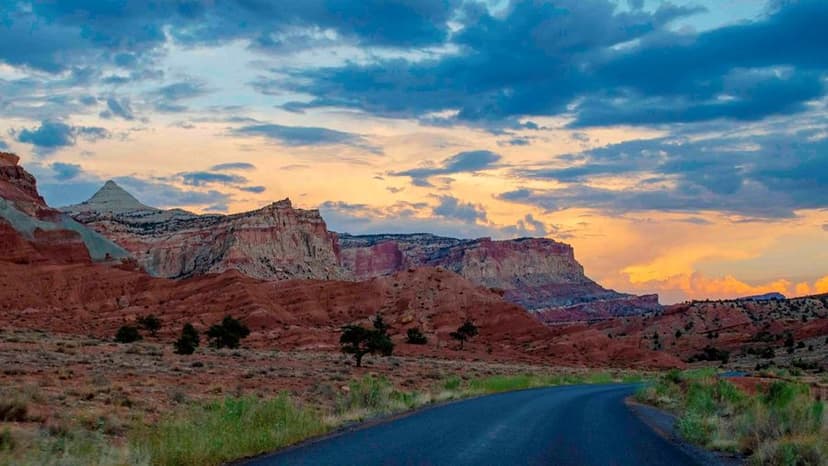 Sunset in a cloudy sky, above red and white cliffs, green grass, and a road