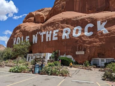 A roadside attraction that is a cliffside painted with the words "Hole N The Rock" behind the attraction's parking lot